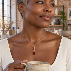 A woman with short gray curls wears the rose gold garnet necklace while holding a ceramic cup in a pottery studio.