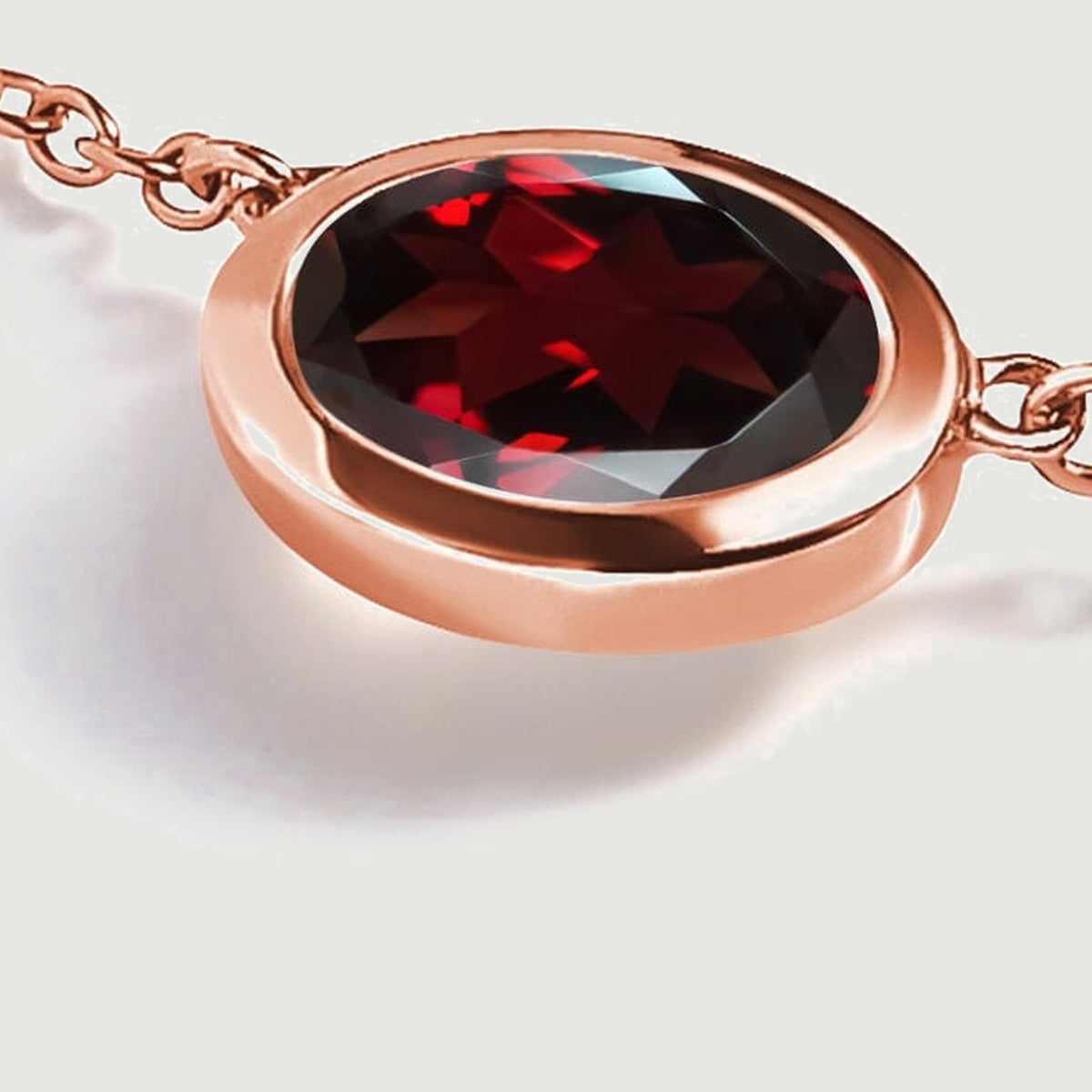 An angled close-up reveals the raised rose gold plated bezel around the oval garnet with chain links extending to both sides.