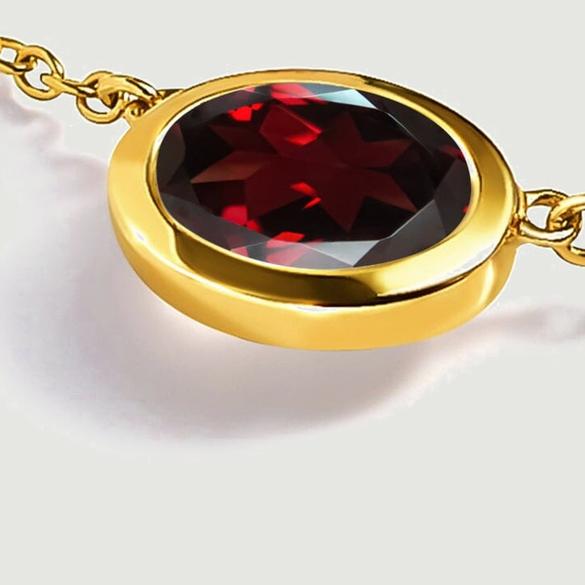 A low angled view shows the thickness of the yellow gold plated setting beneath the red garnet on a light grey surface.