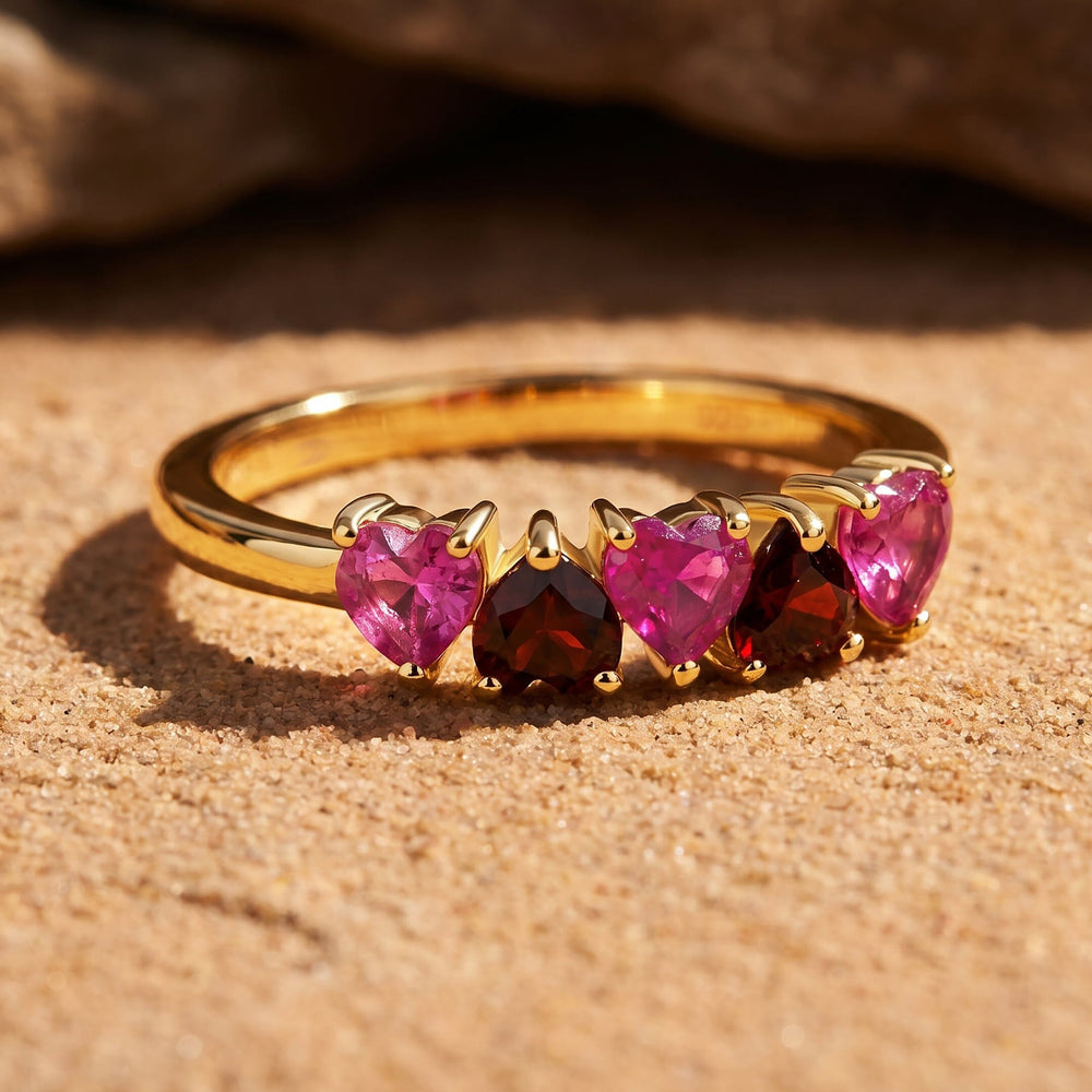 The yellow gold ring rests on a textured beige stone with its heart-shaped gemstones facing forward.