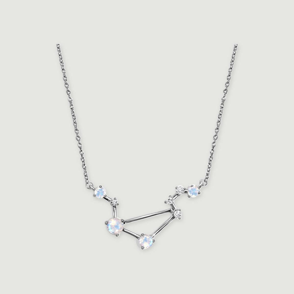 A sterling silver constellation necklace with four pale round moonstones and small clear accents rests on a light gray background.