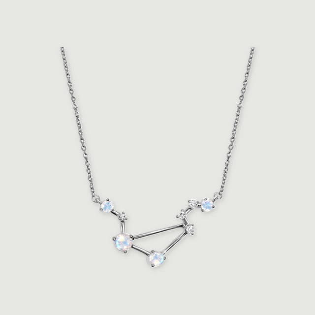 A sterling silver constellation necklace with four pale round moonstones and small clear accents rests on a light gray background.