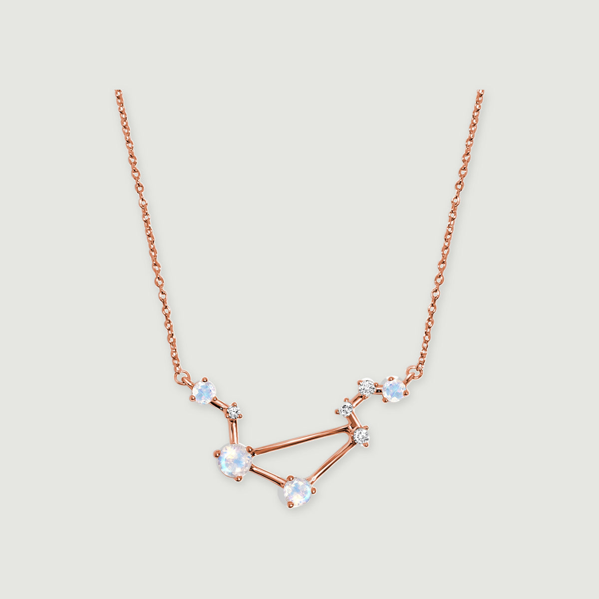 A rose gold vermeil constellation pendant with round iridescent stones is centered on a light gray surface.