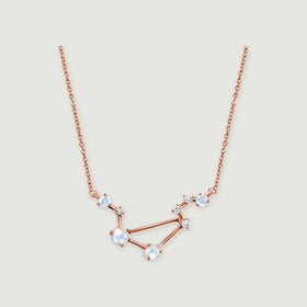 A rose gold vermeil constellation pendant with round iridescent stones is centered on a light gray surface.
