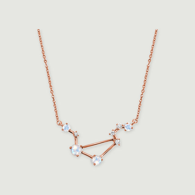 A rose gold vermeil constellation pendant with round iridescent stones is centered on a light gray surface.