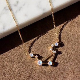 A yellow gold vermeil constellation necklace casts a clear shadow on a tan tabletop below white marble.