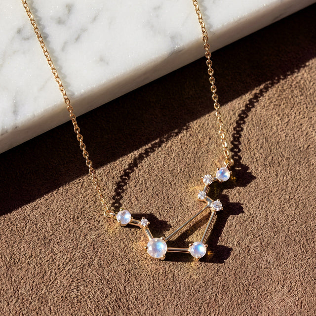 A yellow gold vermeil constellation necklace casts a clear shadow on a tan tabletop below white marble.