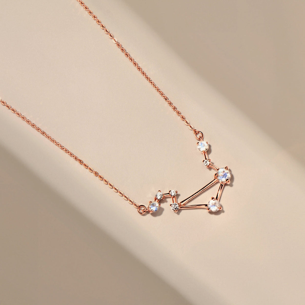 A rose gold vermeil necklace lies diagonally across a smooth cream surface with its pale stones in view.