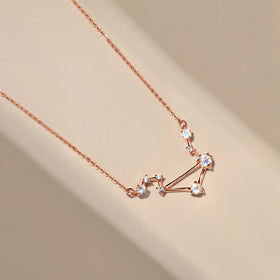 A rose gold vermeil necklace lies diagonally across a smooth cream surface with its pale stones in view.