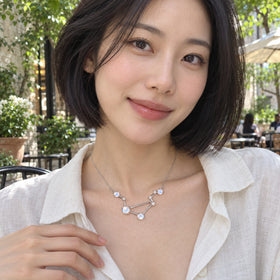 A sterling silver moonstone necklace rests at the collarbone above an ivory linen shirt in a leafy courtyard cafe.