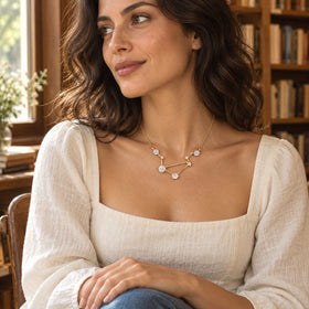 A yellow gold vermeil moonstone necklace is worn with a cream square-neck blouse beside a sunlit bookshop window.