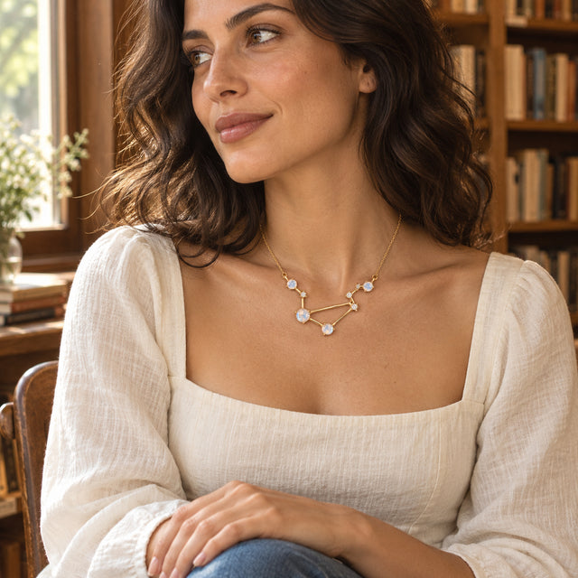A yellow gold vermeil moonstone necklace is worn with a cream square-neck blouse beside a sunlit bookshop window.