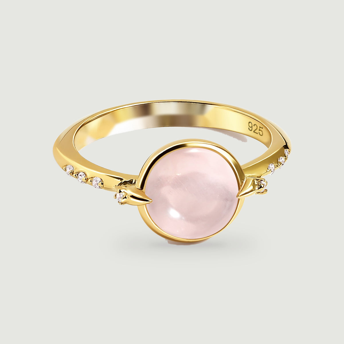 A yellow gold ring displays a pale pink oval cabochon between pointed prongs and clear accent stones.