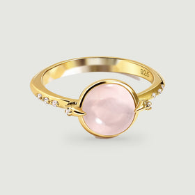 A yellow gold ring displays a pale pink oval cabochon between pointed prongs and clear accent stones.