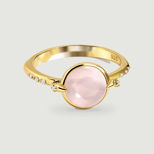 A yellow gold ring displays a pale pink oval cabochon between pointed prongs and clear accent stones.