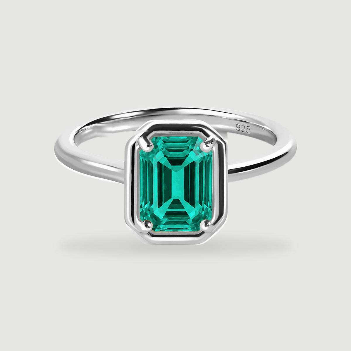 A sterling silver ring with a rectangular green stone is centered on a light grey surface.