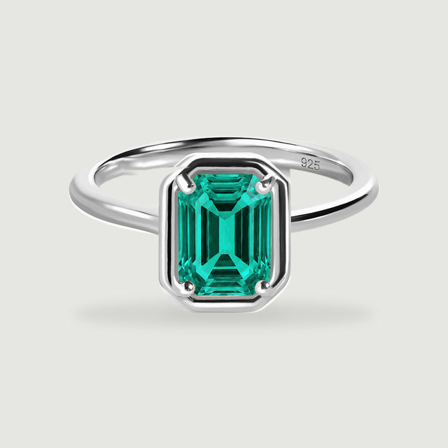 A sterling silver ring with a rectangular green stone is centered on a light grey surface.