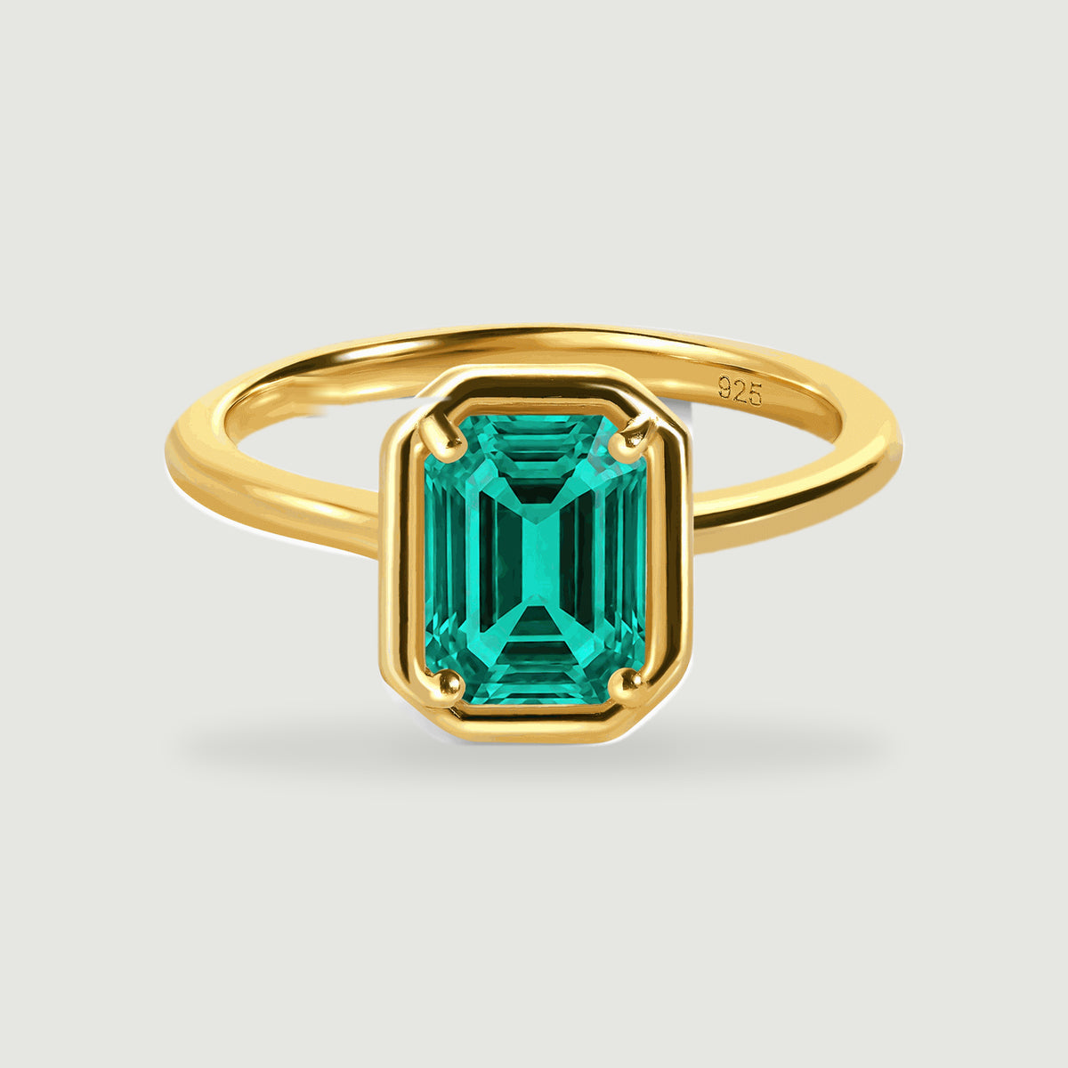 A yellow gold vermeil ring with a rectangular green stone is centered on a light grey surface.