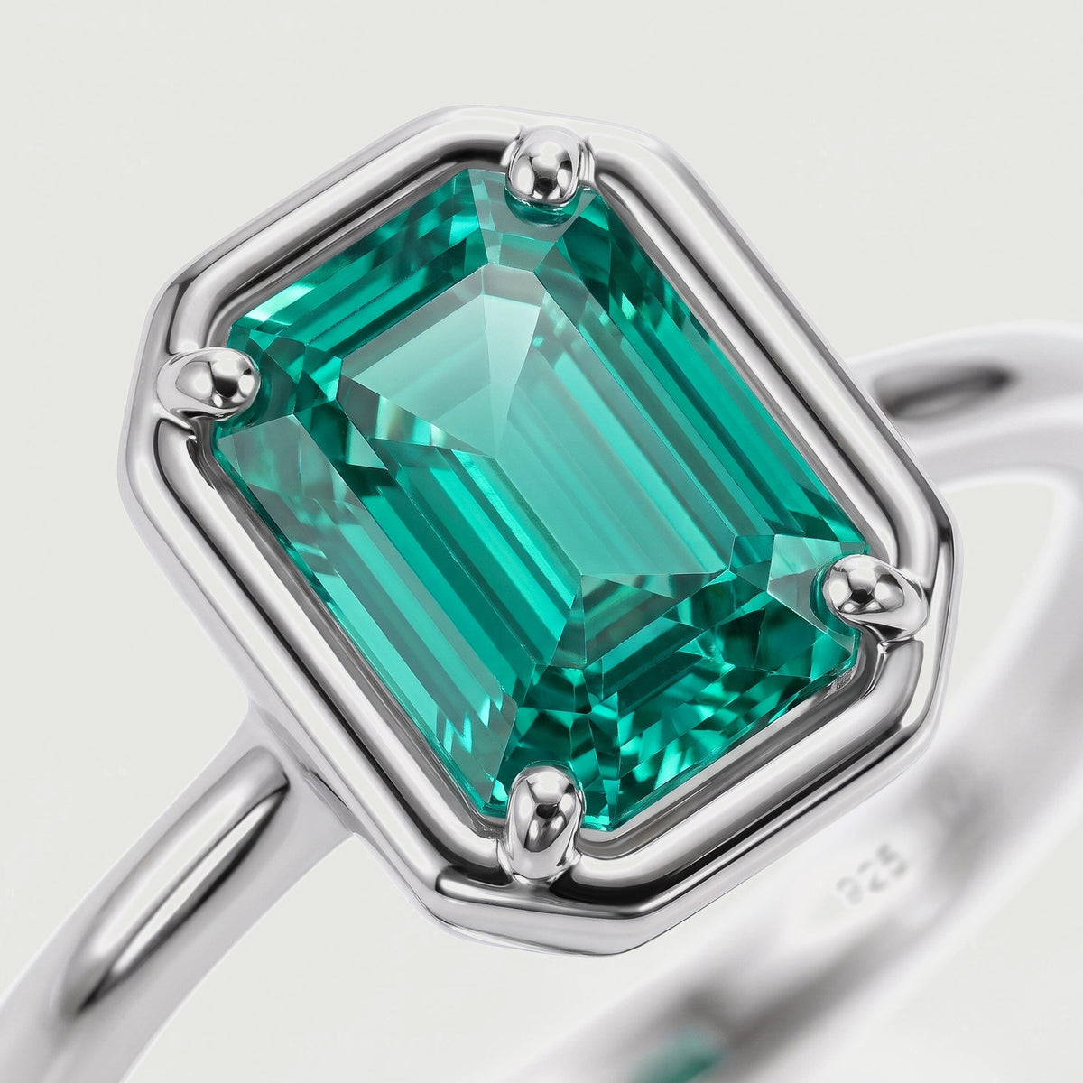 A close view shows the green step-cut stone and four rounded silver prongs.