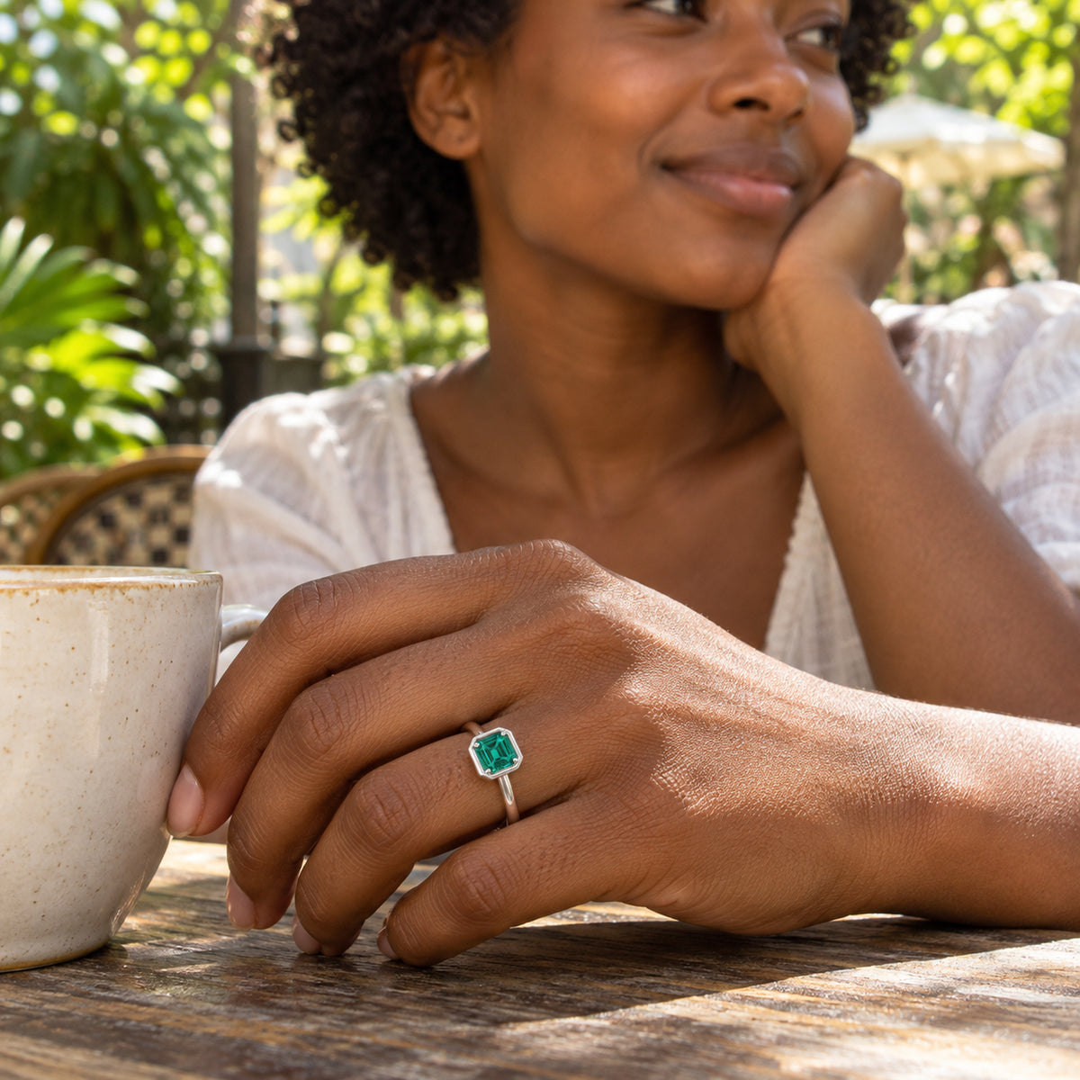 A woman wears the silver green-stone ring while holding a ceramic cup at an outdoor table.