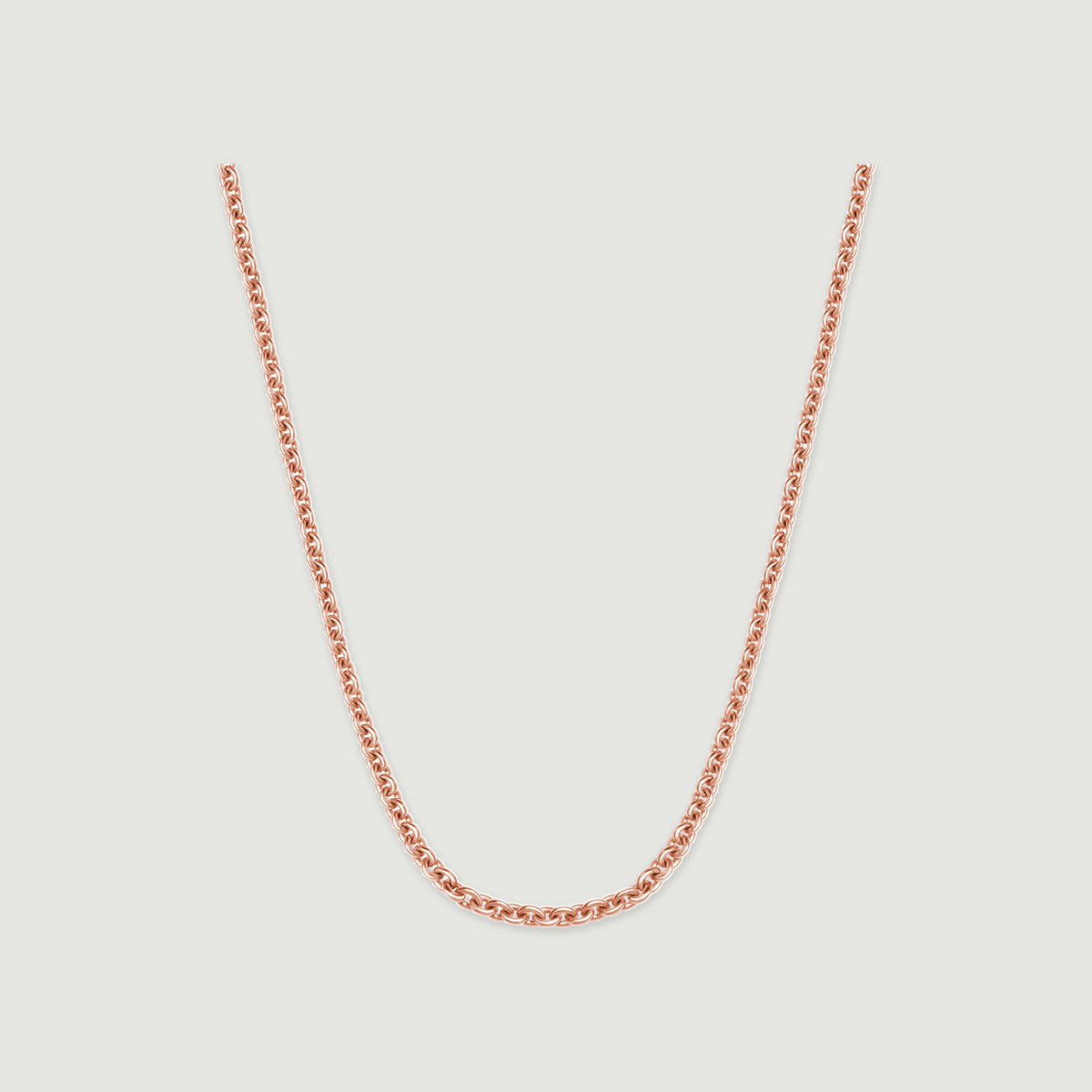 A rose gold chain rests in a broad curve against a pale gray surface.