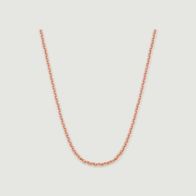A rose gold chain rests in a broad curve against a pale gray surface.