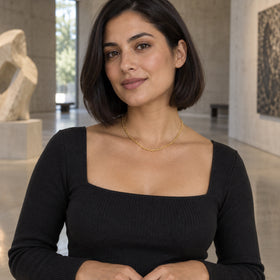 A yellow gold chain sits above a black square neckline in an art gallery.