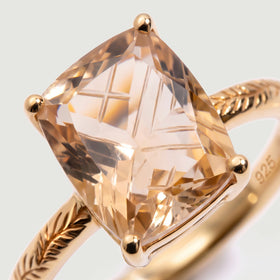 A close view reveals the intersecting cuts of champagne quartz, rounded gold prongs and leaf engraving.