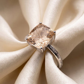 A sterling silver champagne quartz ring rests diagonally across softly folded ivory fabric.