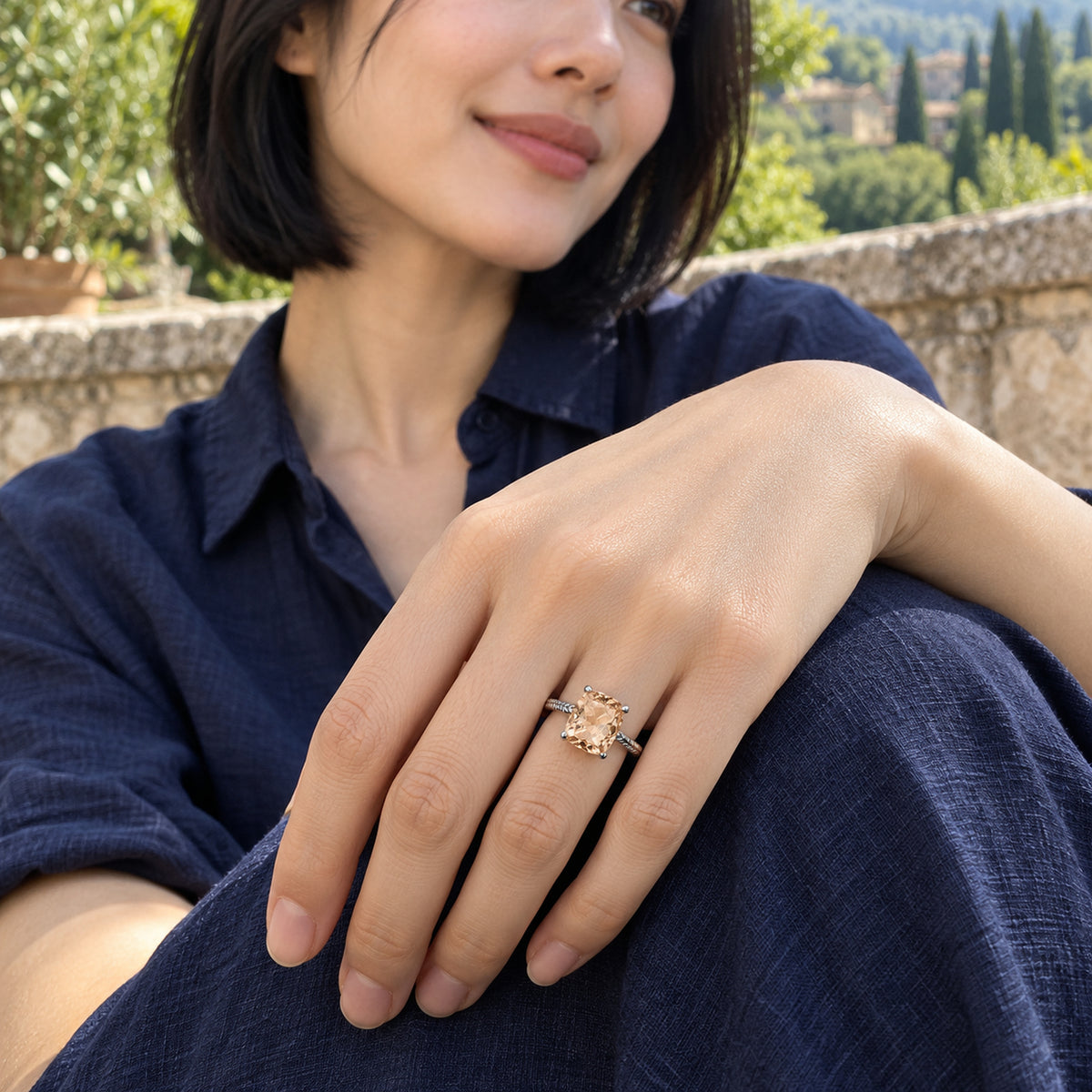 A woman in a navy shirt wears a silver champagne quartz ring with her hand resting on her knee on a leafy stone terrace.