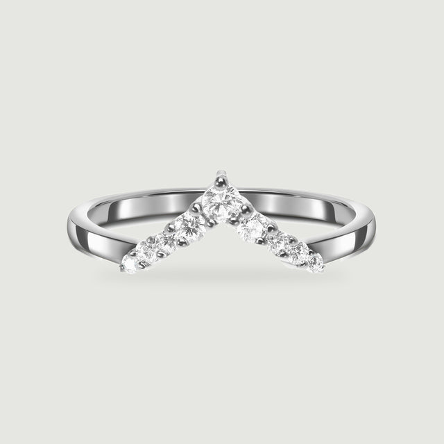 A polished silver chevron ring with round clear stones is centered on a pale gray background.