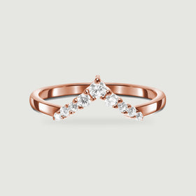 A rose gold chevron band displays clear faceted stones above a soft contact shadow.