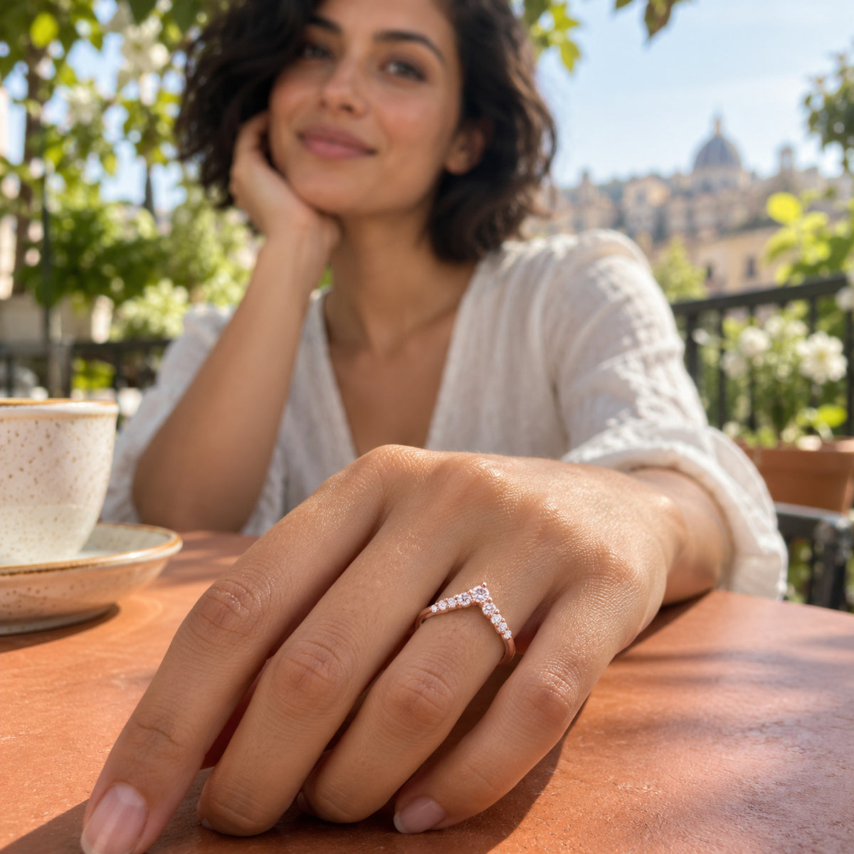 A rose gold chevron ring is worn on a hand resting on a terracotta cafe table.