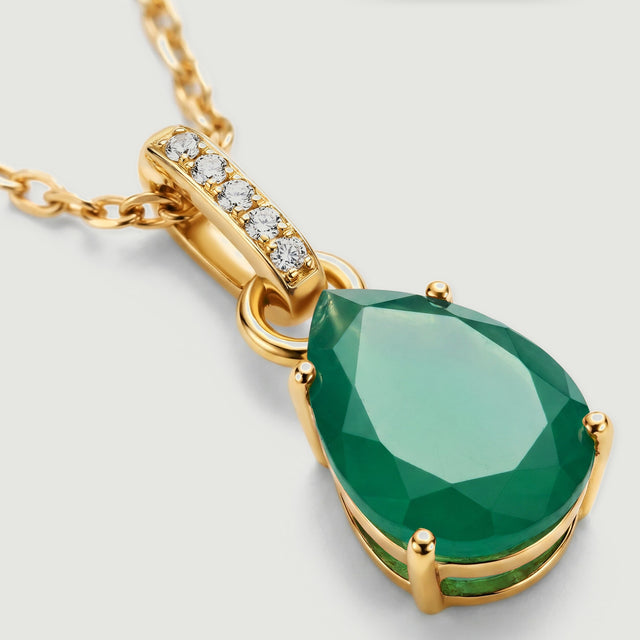 The green stone facets, rounded gold prongs and clear stones are visible in a close-up.