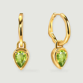 A pair of yellow gold-tone hoops with green pear-shaped pendants casts soft shadows on a pale gray surface.