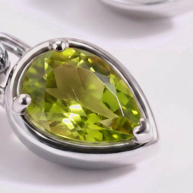 A close view shows the facets and three rounded prongs around a green pear-shaped stone in a silver-tone setting.