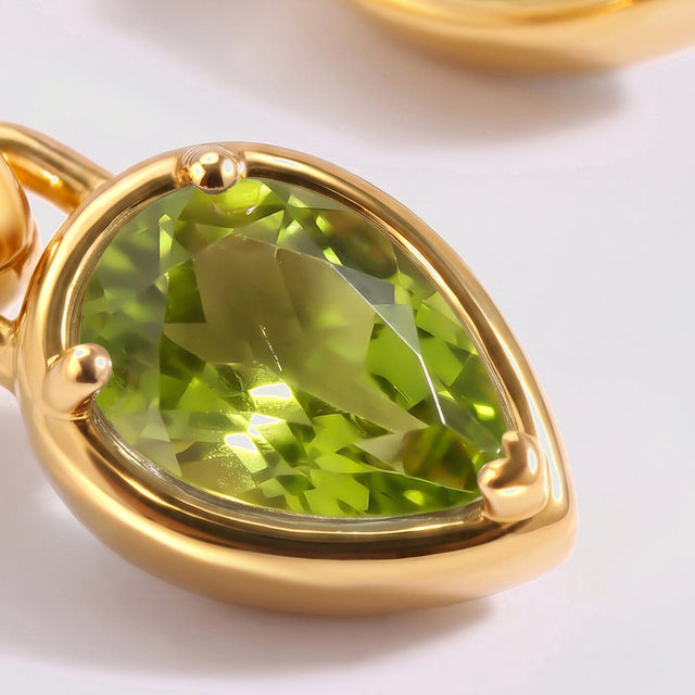 A faceted green peridot drop sits in a polished yellow gold-tone setting beside its connecting loop.