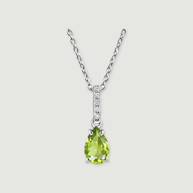 A silver chain meets a narrow white-stone bail above a faceted green pear pendant on a softly shadowed gray background.