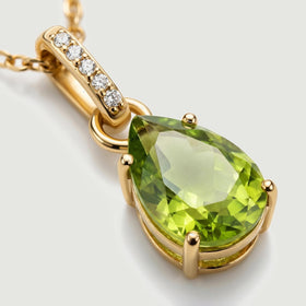A close view shows the green peridot facets, four yellow gold prongs, and five white stones along the curved bail.