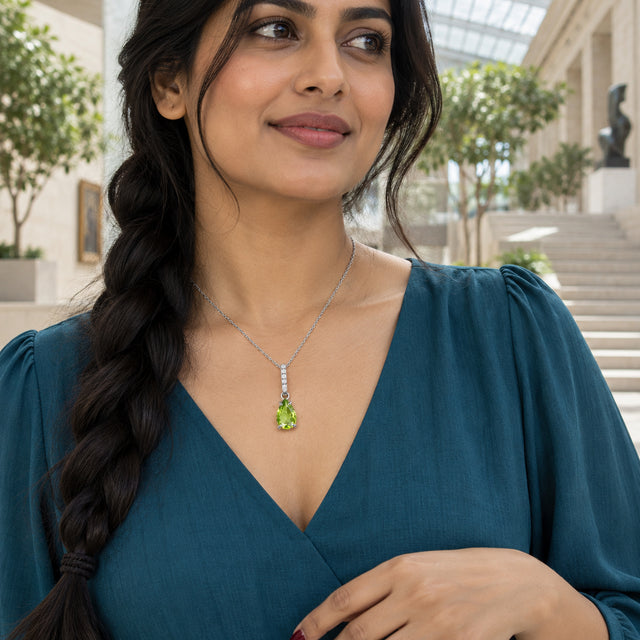 A woman with a dark braid wears the silver peridot necklace above a teal V-neck blouse in a bright gallery.