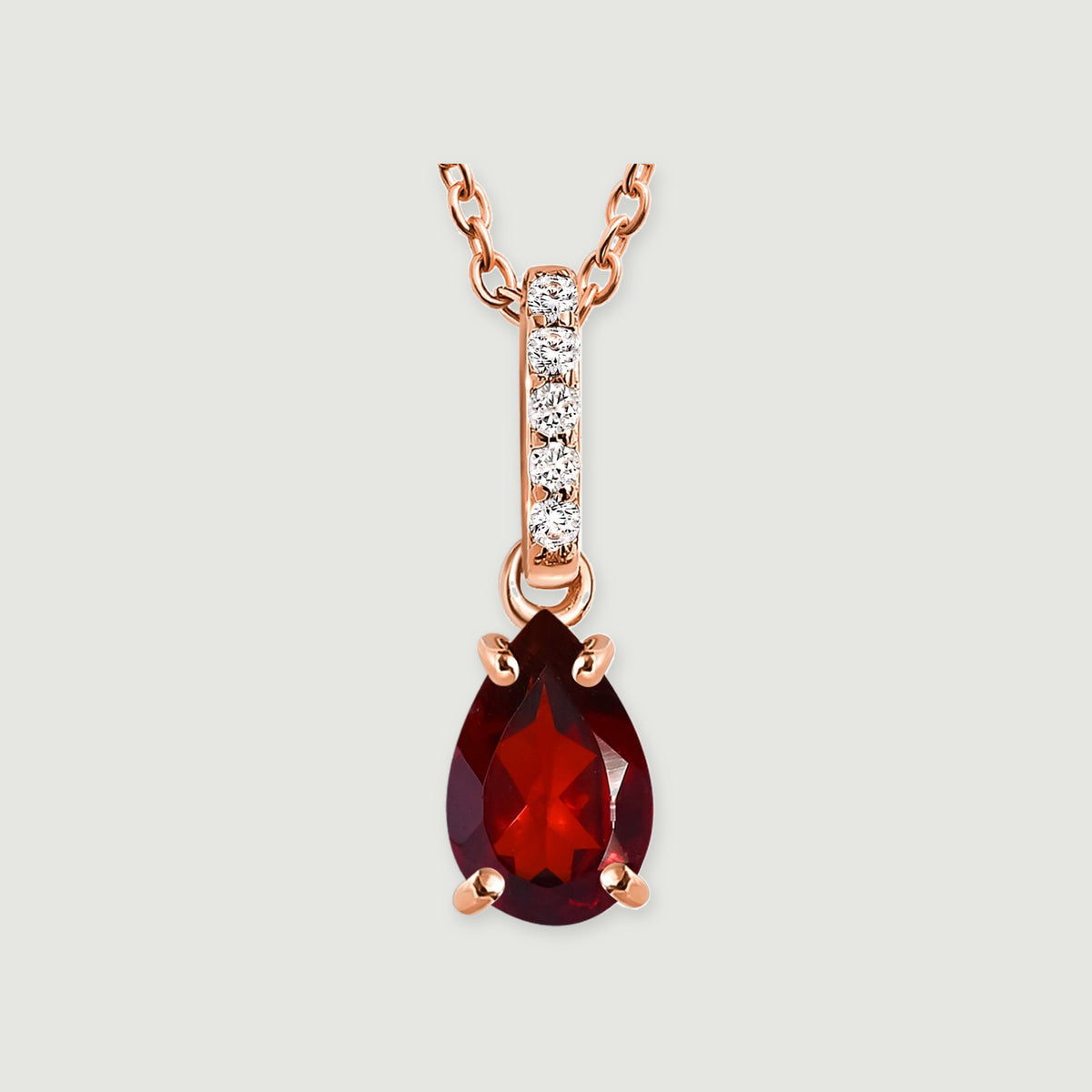 A rose gold vermeil pendant displays a faceted red garnet held by four prongs beneath a sparkling bail.