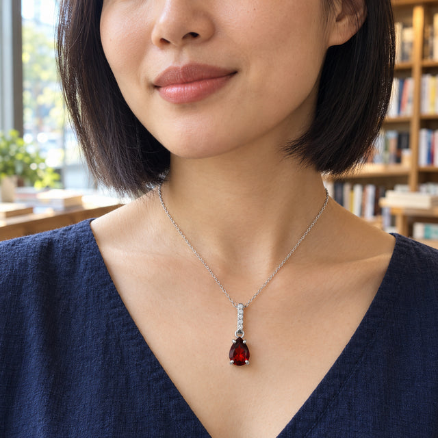 The silver garnet necklace rests above a navy neckline on a woman with a dark bob beside bookshelves.