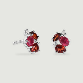 A pair of silver stud earrings shows bright polished prongs around pink and red gemstones with clear round accents.