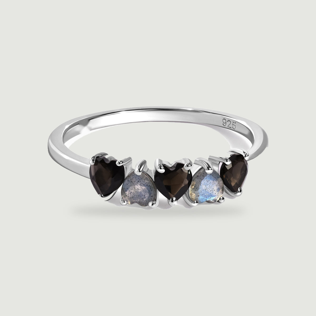 A sterling silver ring with five alternating black and blue-gray heart-shaped stones is centered on a pale gray background.
