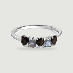 A sterling silver ring with five alternating black and blue-gray heart-shaped stones is centered on a pale gray background.