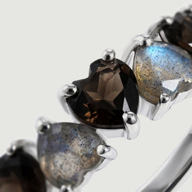 A close view reveals a faceted black heart beside a blue-flashing gray heart held by polished silver prongs.