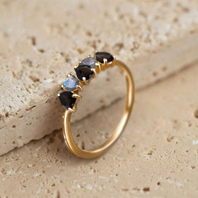 A yellow gold vermeil ring leans against a pale textured stone surface with its five heart-shaped gems visible.