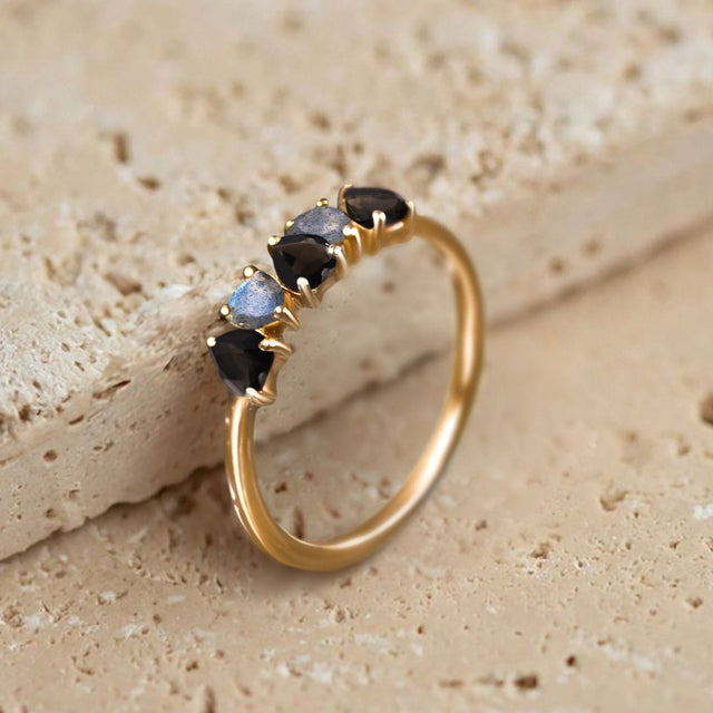 A yellow gold vermeil ring leans against a pale textured stone surface with its five heart-shaped gems visible.