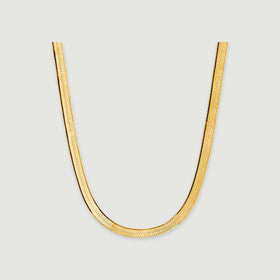 A flat yellow gold herringbone necklace curves into a U shape on a light gray surface.