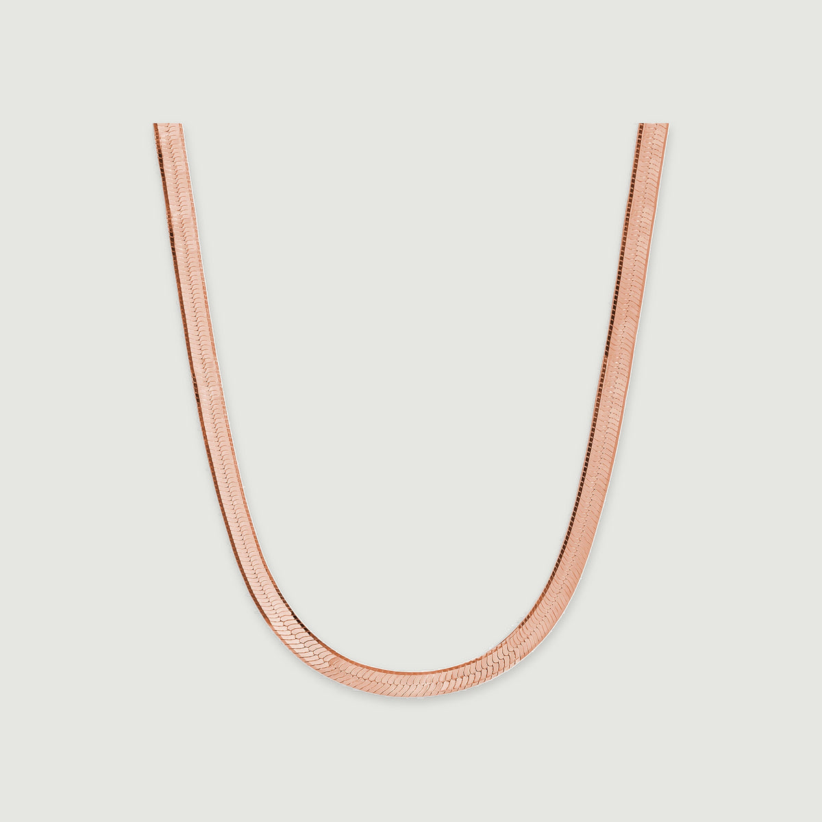 A rose gold herringbone chain displays closely fitted links against a pale gray background.